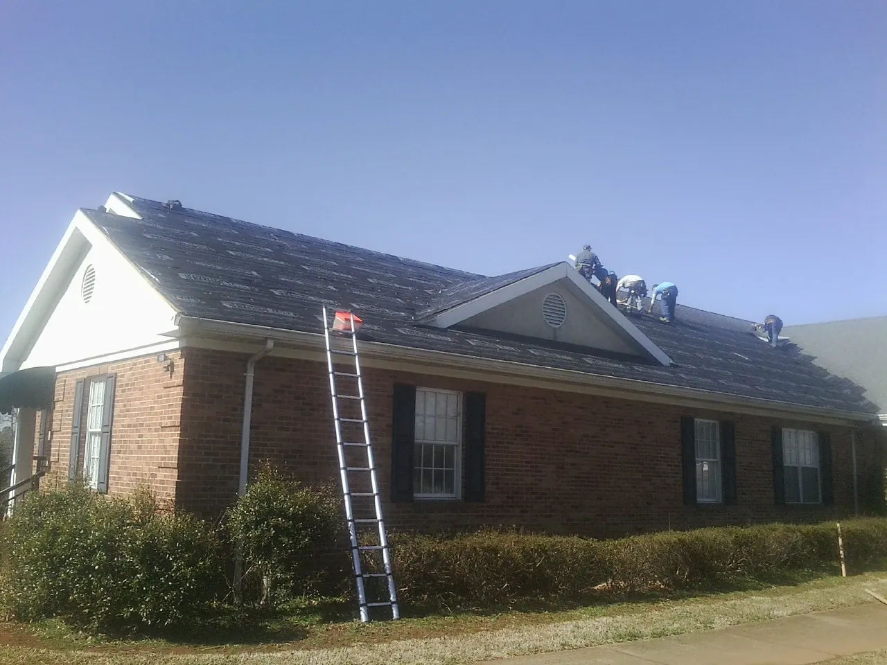 Crew tearing shingles off a brick ranch roof with a ladder set — Emergency Roof Repair work by our crew in New Philadelphia