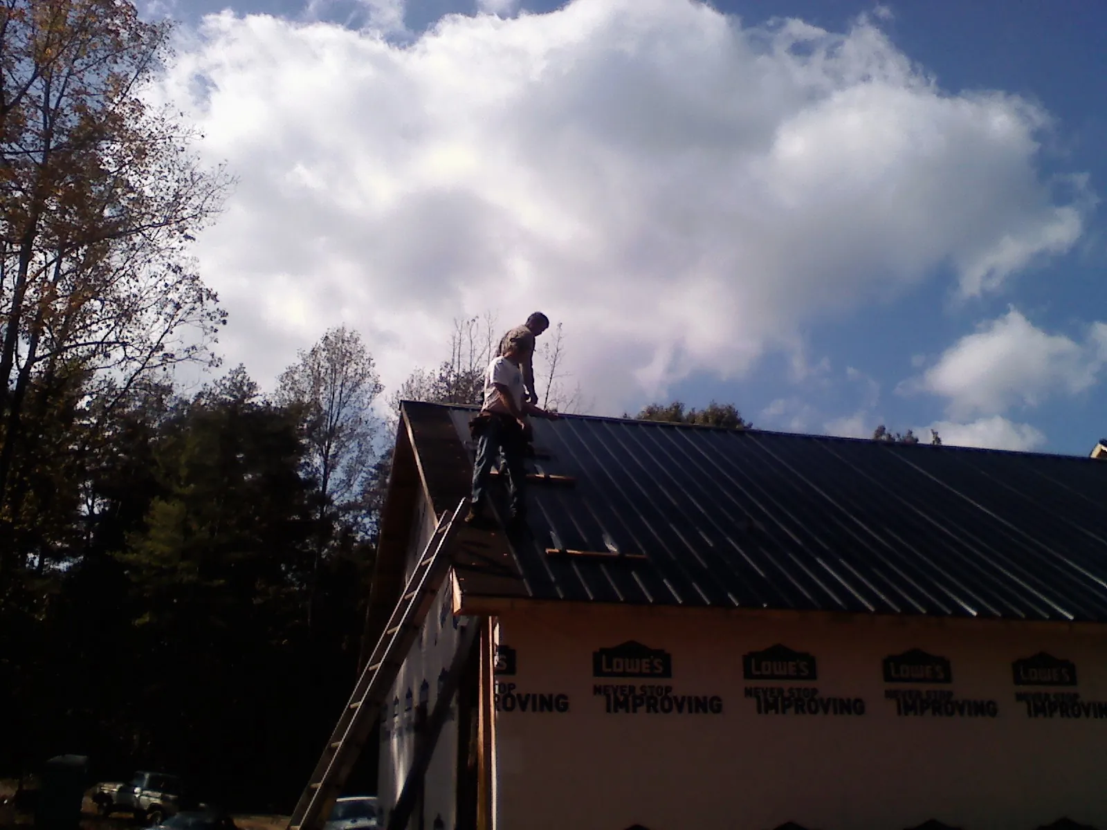 Roofer fastening dark metal panels high against a cloudy sky, from a Roof Inspection job in New Philadelphia