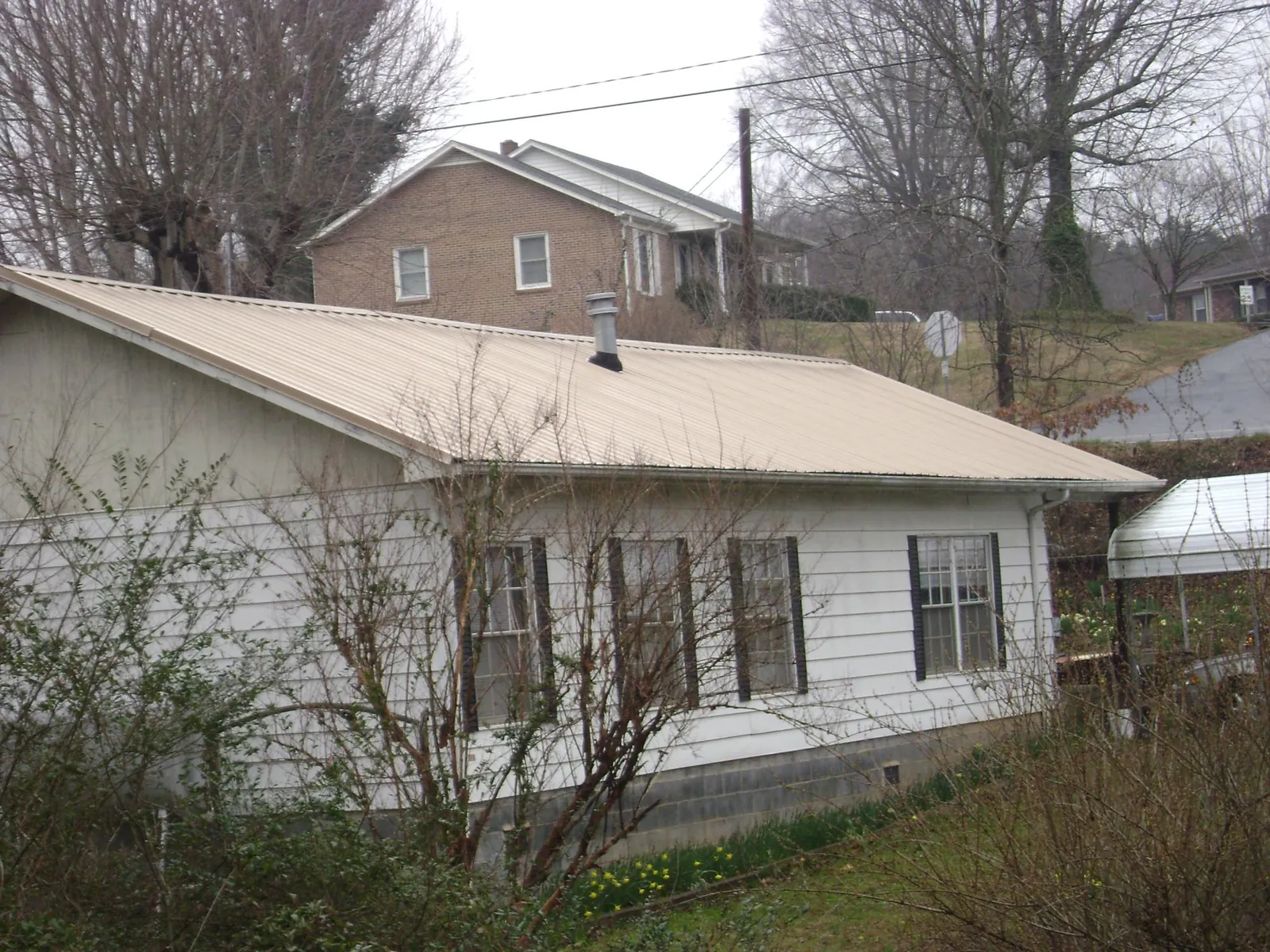 Tan metal roof on a white sided house set into a hillside — Commercial Roofing by Roofing Brothers in New Philadelphia